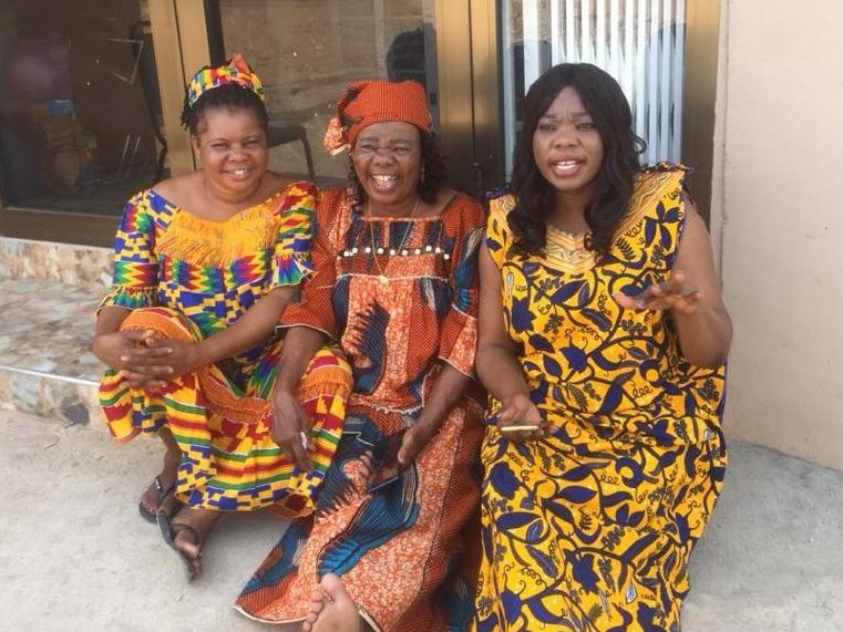 Three women in brightly patterned dresses sitting together and smiling