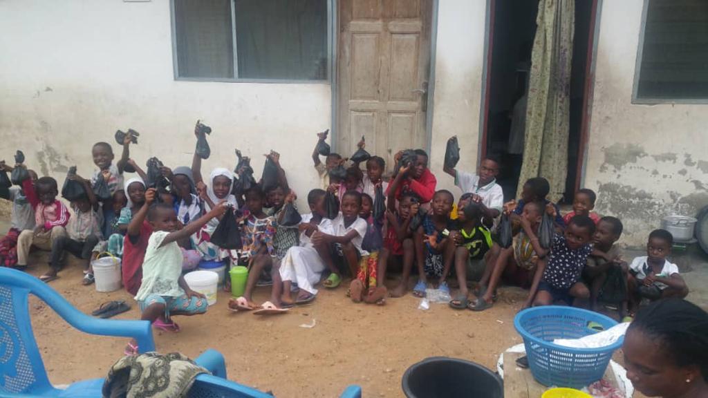 Children and adults sitting together in the shade outside a school building