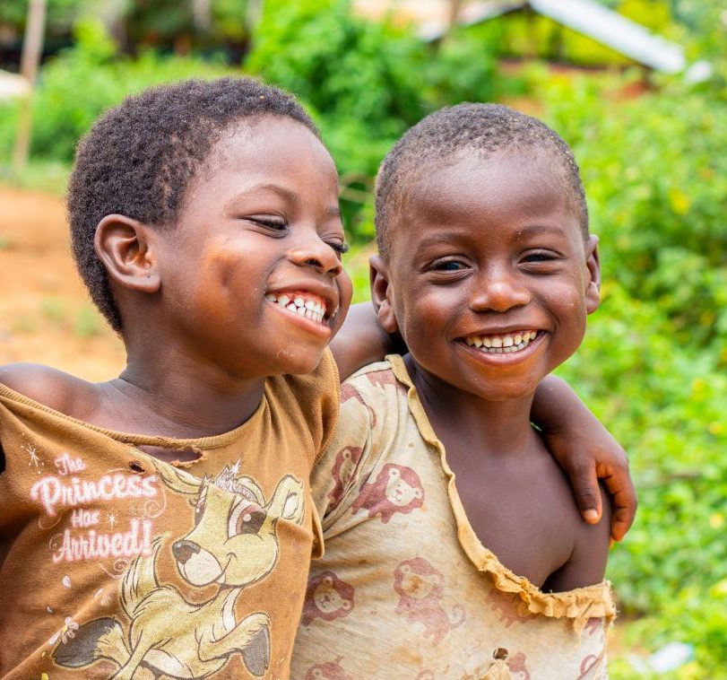 Two young children smiling, arm in arm, outdoors