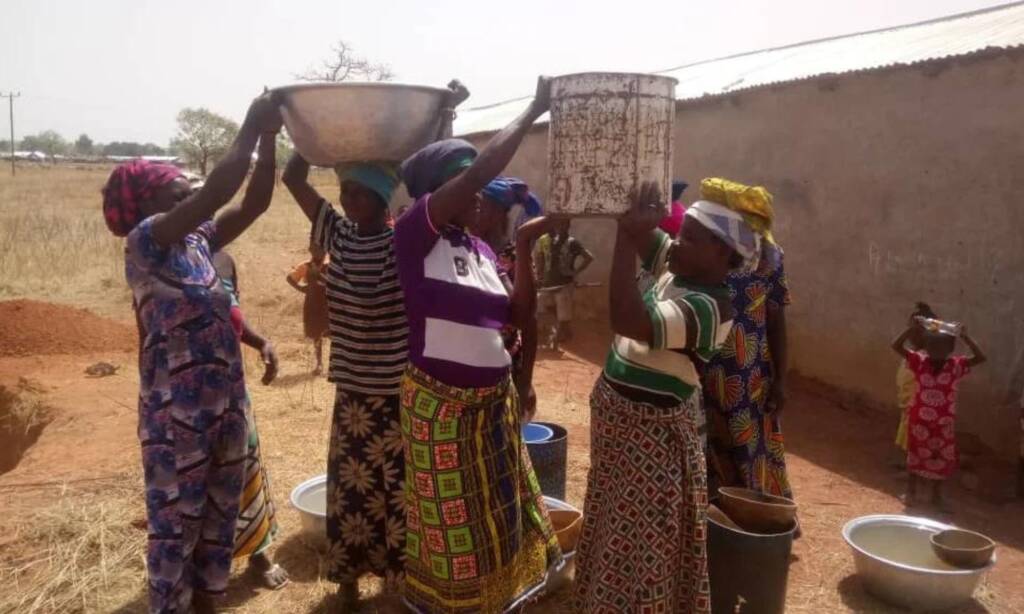 Women carrying bowls on their heads beside a village wall