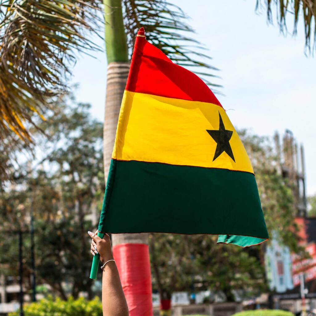 The flag of Ghana held aloft by a raised hand under palm trees