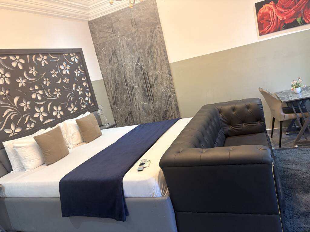 A guest room with a carved floral headboard panel, a navy bed runner and a tufted grey sofa