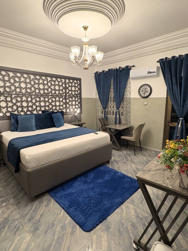 A guest room with blue curtains, a lattice headboard panel and a chandelier