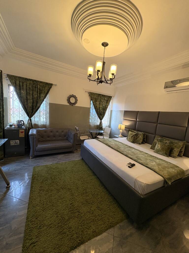 A guest room with a green bed runner, a green rug and a grey sofa